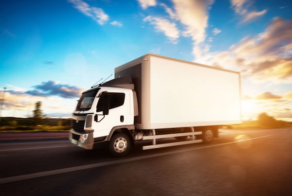 Commercial cargo delivery truck with blank white trailer driving on highway. Generic, brandless vehicle design. 3D rendering